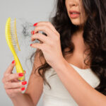 a woman holding a brush with hair ผมร่วง